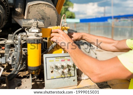 Driver mechanic changes oil in a compactor at a construction site, close-up