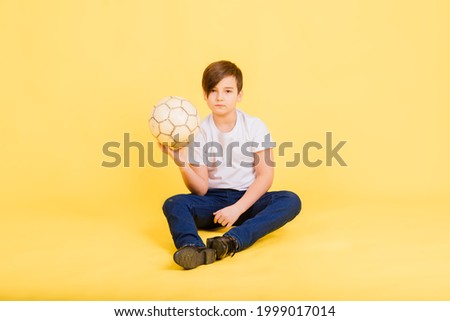 Portrait of a boy holding soccer ball, studio yellow background