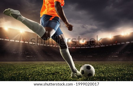 Cropped male soccer, football player practicing, attacking, kicking ball at sport match on sky background at stadium with flashlights. Sport competition. Action, motion, energy and dynamic concept.
