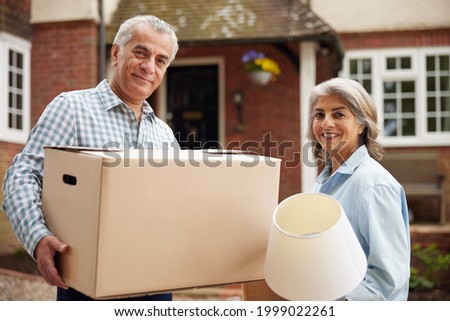 Portrait Of Mature Couple Carrying Boxes On Moving Day In Front Of Dream Home Royalty-Free Stock Photo #1999022261