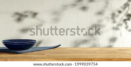 Wooden board of free space for your decoration and blue plate with napkin. White wall with shadows and sun light 
