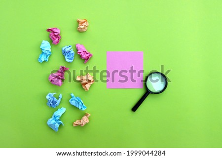 Top view photo of a magnifying glass and blank sticker on a green background.