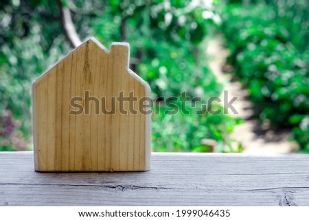Wooden toy house on blurry background of garden. Symbol of village life, living in private house, selling suburban real estate.
