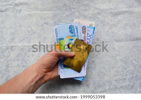 in a man's hand, on a white fabric background, credit bank cards and Russian rubles of various denominations