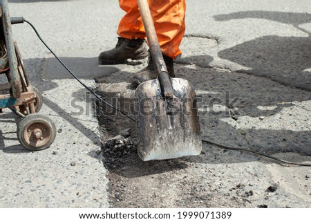 Shovel with asphalt. Repair of the road. Tool for cleaning old asphalt. A worker cleans the road from asphalt with a shovel.