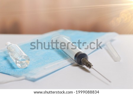 In the photo, the color background on it is a medical mask, a syringe and an ampoule. The concept of vaccination of the population.