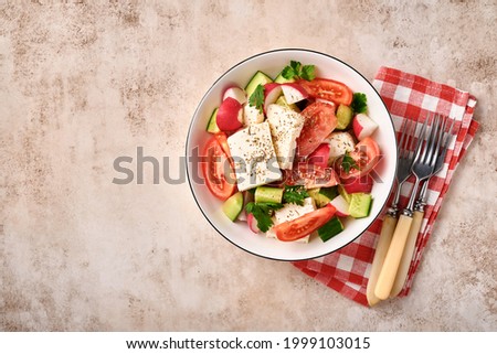 Radish, cucumber, tomato, pepper and feta cheese with spices pepper and olive oil in white bowl on grey slate, stone or concrete background. Healthy food concept. Top view.