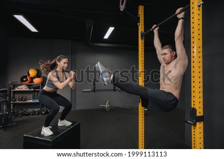 Crossfit training. Handsome shirtless muscular man doing abdominal exercise while fit sporty woman doing box jump exercise. Functional training workout, group circuit training, fitness class Royalty-Free Stock Photo #1999113113