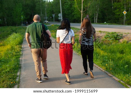 A guy and two girls are walking along the road. Young people are walking down the street. Three people shot from the back. Walk of young people around the city.