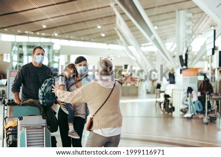 Senior woman welcoming her daughter and family  with open arms at airport arrival gate. Traveler family of three welcomed by grandma at airport in pandemic. Royalty-Free Stock Photo #1999116971