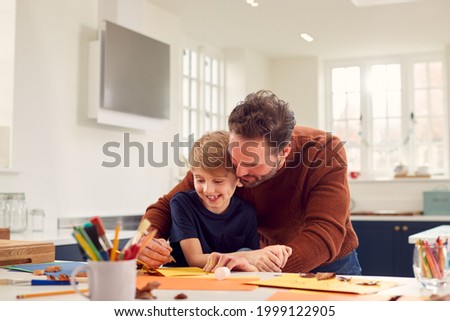 Father With Son At Home Doing Craft And Making Picture From Leaves In Kitchen