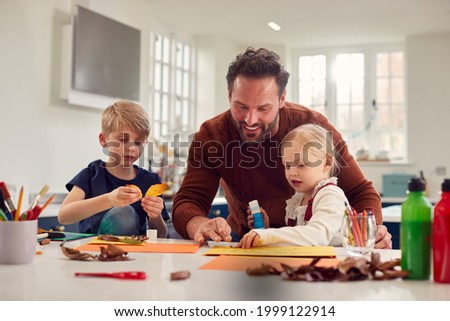 Father With Children At Home Doing Craft And Making Picture From Leaves In Kitchen