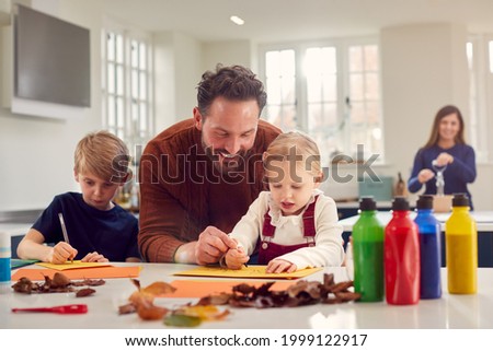 Father With Children At Home Doing Craft And Making Picture From Leaves In Kitchen