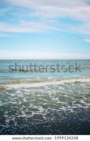 Sandy seashore view with waves, foam and blue cloudy sky.