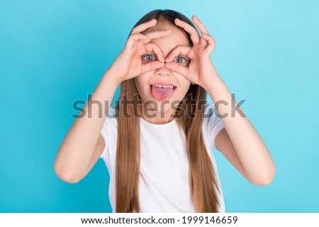 Photo of funny brown hair little girl hands eyewear tongue out wear white t-shirt isolated on blue color background