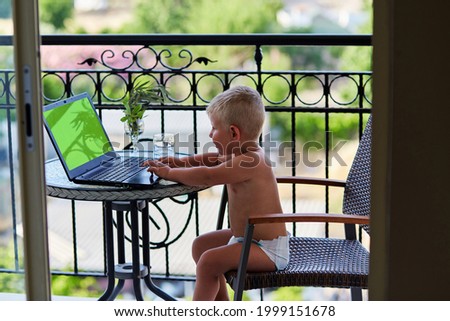 Caucasian toddler boy in diaper plays on laptop on terrace on sunny day. Chromackey screen laptop. New generation of children. Playing games, watching cartoons in front of mountain view. quality photo
