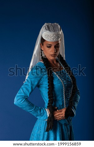 Beautiful authentically dressed brunette Georgian girl posing looking down. High quality picture of authentic Caucasian dancers performing on dark blue matte background