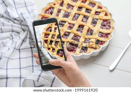 Female food photographer with mobile phone taking picture of tasty cranberry pie