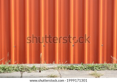 Orange metal sheet walls and grassy concrete pavement.