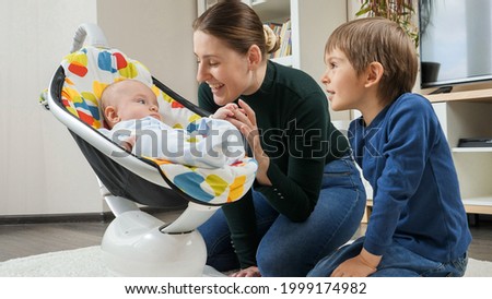 Cute smiling baby boy rocking in chair and looking at mother ond older brother. Child development and happy childhood Royalty-Free Stock Photo #1999174982