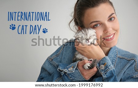 Young woman with cute little kitten on grey background. International Cat Day Royalty-Free Stock Photo #1999176992