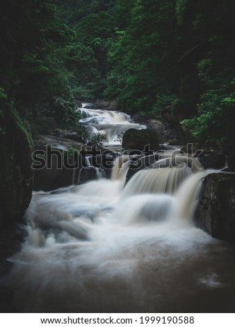 Breathtaking wide angle shot of powerful stream waterfall with big rock in lush rainforest surrounding. Long exposure. Leaves moving, low speed shutter blur. Nakhon Nayok, Thailand.