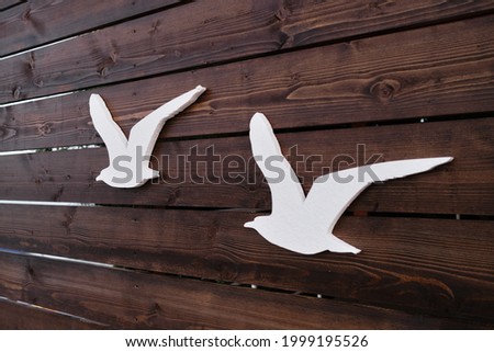 Couple of birds are flying south. Creative minimalistic advertising of sea cafe, sign and banner with seagull. Silhouettes of figures of artificial gulls on wooden background.