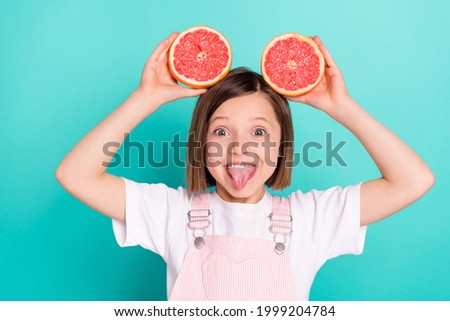 Photo of pretty adorable schoolgirl dressed pink overall holding grapefruit slices showing tongue isolated turquoise color background