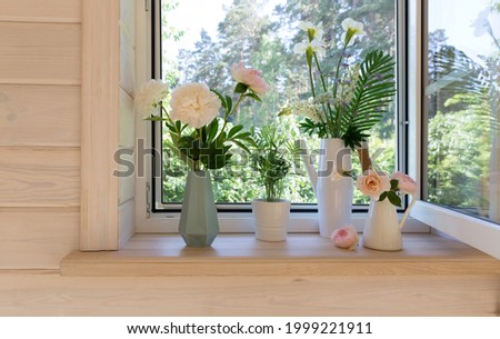 White window with mosquito net in a rustic wooden house overlooking the garden. Bouquet of white irises and lupins in watering can on the windowsill