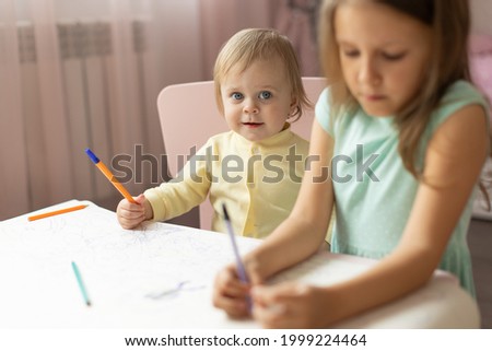 two children draws at the table in the room, one year old and six years old 