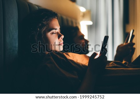 Couple with smartphones in their bed. Mobile phone addiction. Bored distant couple ignoring each other lying in bed at night while using mobile phones.