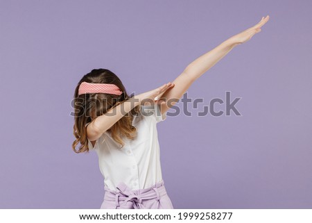 Little kid girl 12-13 years old in white shirt doing dab hip hop dance hands move gesture youth sign hide cover face isolated on purple background children studio portrait. Childhood lifestyle concept