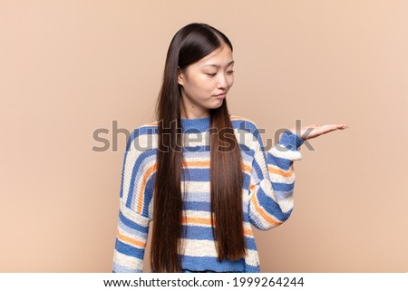 asian young woman feeling happy and smiling casually, looking to an object or concept held on the hand on the side