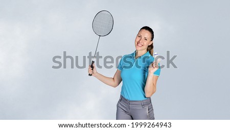 Portrait of caucasian female badminton player holding racket smiling against grey background. sports competition and tournament concept