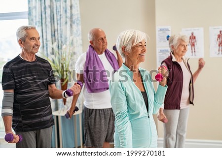 Group of old happy people using dumbbells for workout session at nursing home. Group of senior men and women exercising with dumbbells at gym of care centre. Eldelry doing workout using weights. Royalty-Free Stock Photo #1999270181