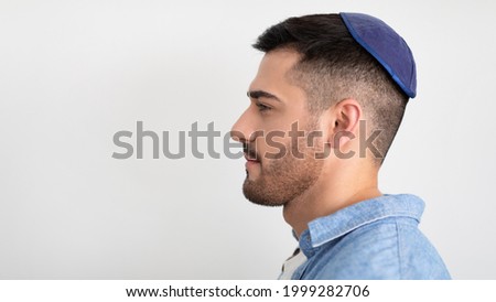 Male Portrait. Profile side view of serious jewish man standing and posing at studio, looking aside at free copy space, wearing blue kippa, posing isolated over white gray studio background, banner Royalty-Free Stock Photo #1999282706
