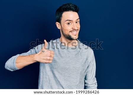 Young hispanic man wearing casual clothes doing happy thumbs up gesture with hand. approving expression looking at the camera showing success. 