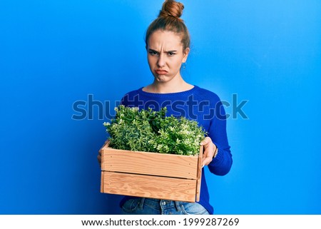 Young blonde woman holding wooden plant pot skeptic and nervous, frowning upset because of problem. negative person. 