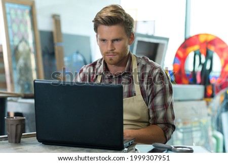 young bearded carpenter using laptop in workshop
