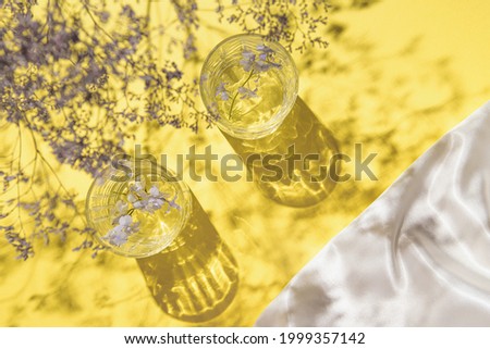 Two glasses with water on yellow background with white silk cloth and shadows. Summer refreshment concept. Sunlit flat lay. Minimal style. Top view