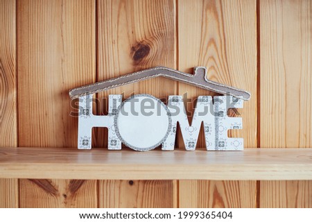 On the background of wooden boards inscription Home with a roof over the words. Cozy photo of an imitation of a house on a wooden background. Welcome home