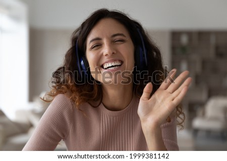 Headshot portrait of smiling millennial Latino female in earphones wave greet talk speak on video call at home. Profile picture of happy young Hispanic woman have webcam online virtual event.
