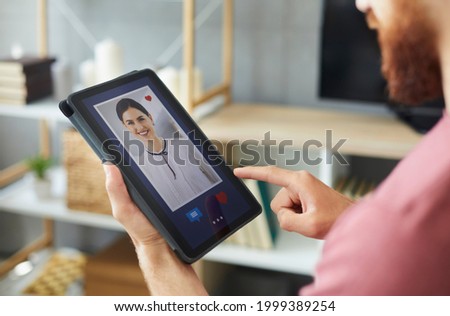 Closeup of young guy looking at photo of pretty woman on tablet display. Close up of man presses red heart like button and sends message to beautiful girl on modern online dating website or mobile app