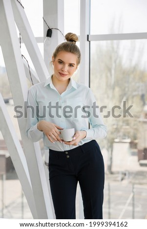 Young beautiful businesswoman or student drinks coffee during a break in the modern office. Relaxation concept 