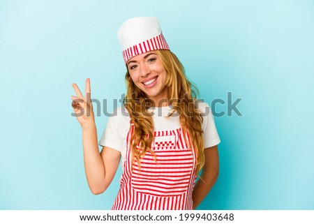 Caucasian ice cream maker woman isolated on blue background  joyful and carefree showing a peace symbol with fingers.