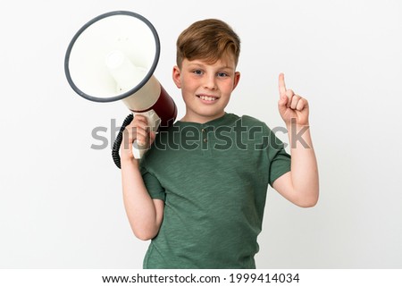 Little redhead boy isolated on white background holding a megaphone and pointing up a great idea