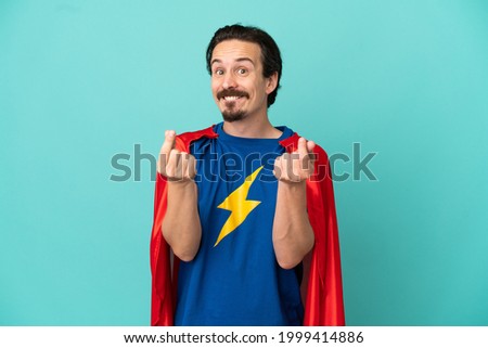 Super Hero caucasian man isolated on blue background making money gesture
