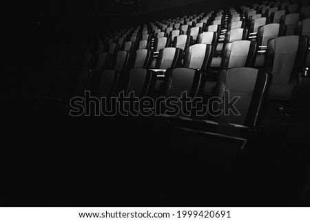 black and white photo, empty cinema. The red and black armchairs in the cinema hall are illuminated by a beam of light, a low key. Selective focus. Quarantine, restrictive tape on chairs  Royalty-Free Stock Photo #1999420691