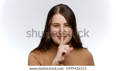 SMiling young woman saying hush and putting finger at lips. Concept of keeping secret and silence