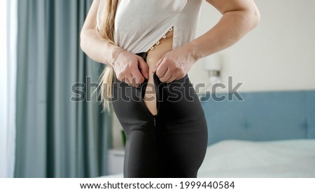 Young woman struggling to xip up tight dress. Concept of excessive weight, obese female, dieting and overweight problems. Royalty-Free Stock Photo #1999440584